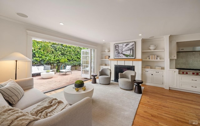 living area with a glass covered fireplace, recessed lighting, ornamental molding, and light wood finished floors
