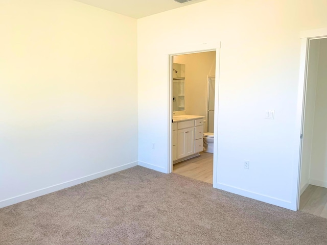 unfurnished bedroom with baseboards, light colored carpet, and ensuite bath