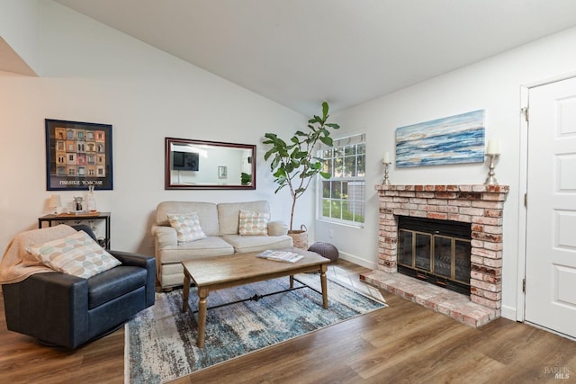 living area featuring a brick fireplace, baseboards, wood finished floors, and lofted ceiling