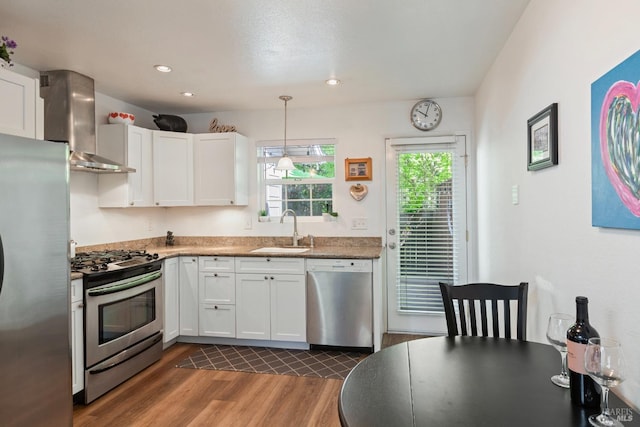 kitchen featuring dark wood-style flooring, wall chimney range hood, white cabinets, a sink, and stainless steel appliances