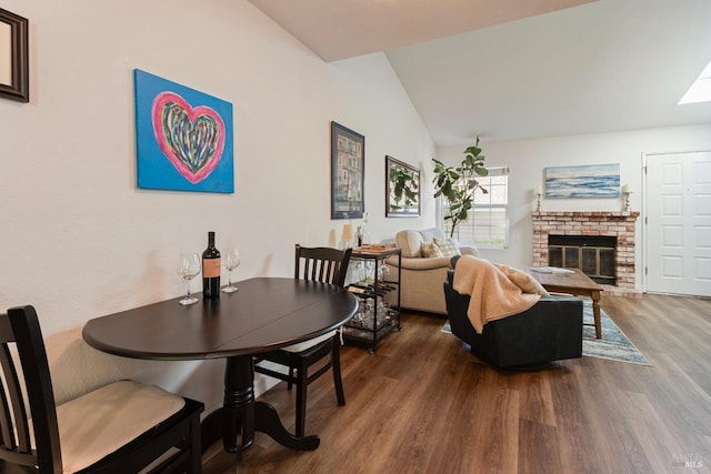 dining area featuring a brick fireplace, lofted ceiling, and wood finished floors
