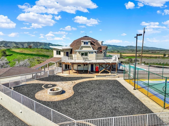 back of property with a deck with mountain view, a fenced backyard, a patio area, a swimming pool, and a fire pit