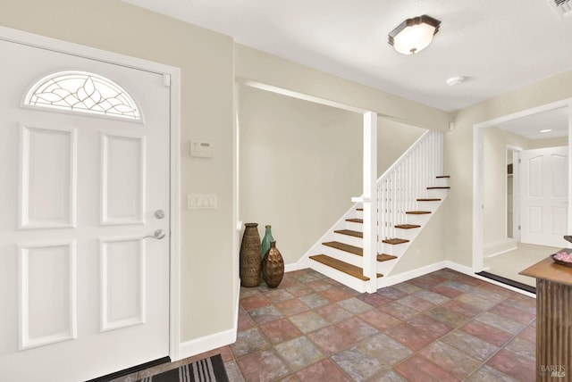 entrance foyer featuring baseboards, stone finish flooring, and stairway