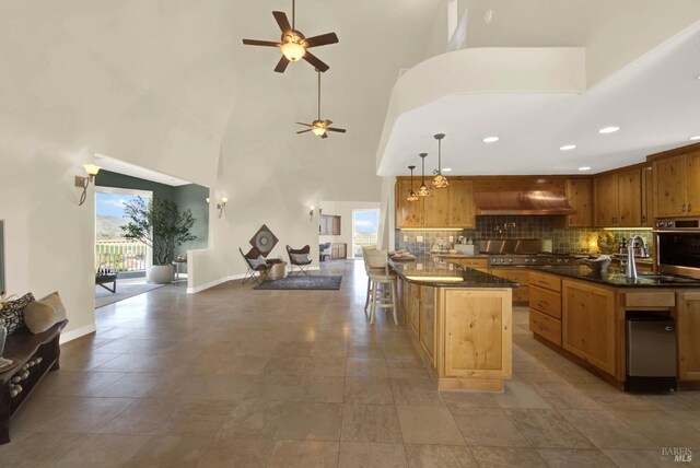 kitchen featuring tasteful backsplash, a sink, a ceiling fan, open floor plan, and a towering ceiling
