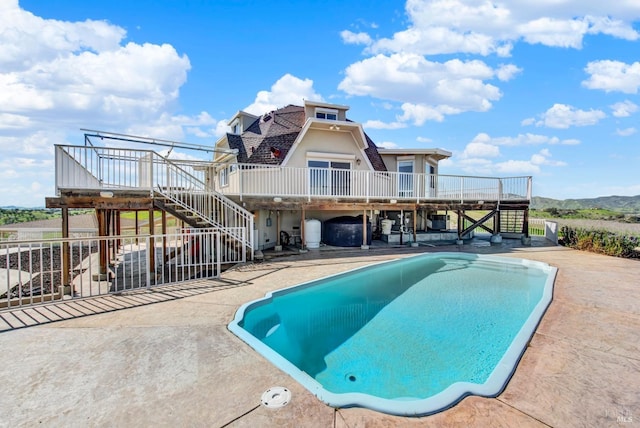 outdoor pool featuring a wooden deck, stairway, and a patio