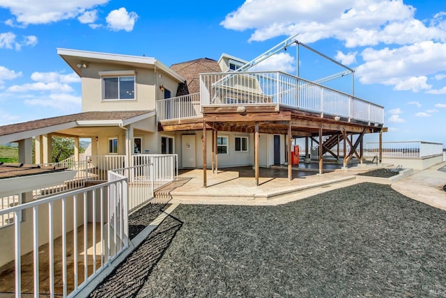 rear view of house with a wooden deck, stairs, stucco siding, and a patio area