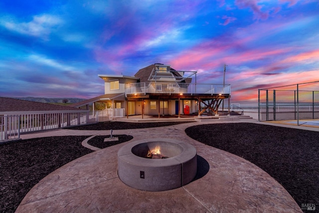 back of house at dusk with a wooden deck, fence, a patio area, an outdoor fire pit, and stairway