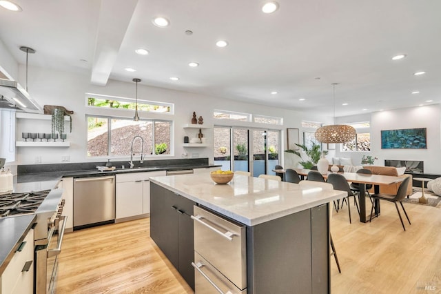 kitchen featuring a kitchen island, decorative light fixtures, appliances with stainless steel finishes, open shelves, and a sink