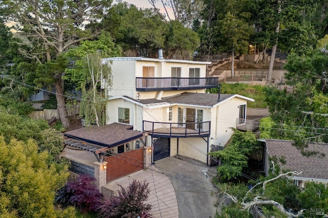 view of front of house with fence, a balcony, concrete driveway, an attached garage, and stucco siding