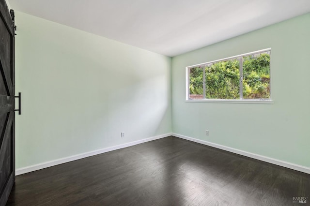 spare room with baseboards, dark wood-style flooring, and a barn door