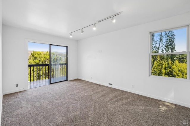 carpeted empty room featuring track lighting, baseboards, and visible vents