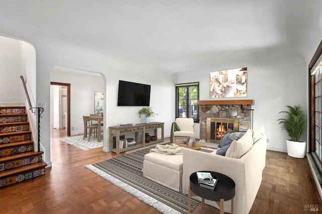 living area with arched walkways, stairs, and a stone fireplace
