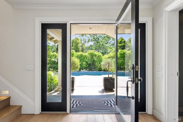 doorway to outside featuring crown molding, wood finished floors, and stairway
