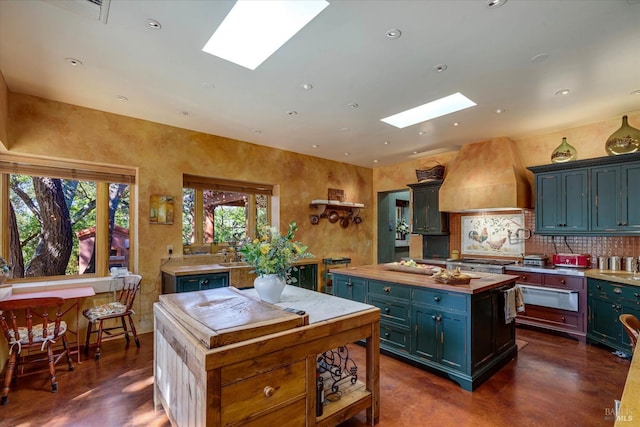 kitchen featuring a kitchen island, tasteful backsplash, custom range hood, a warming drawer, and a skylight