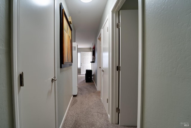 hall featuring carpet floors, baseboards, and a textured wall
