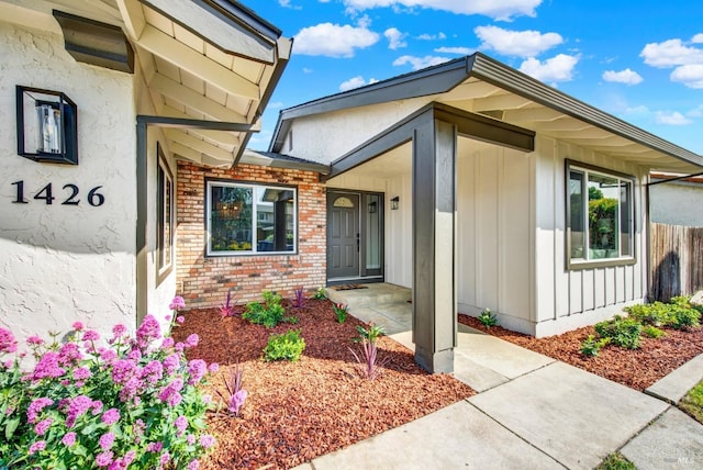entrance to property featuring stucco siding, brick siding, and fence