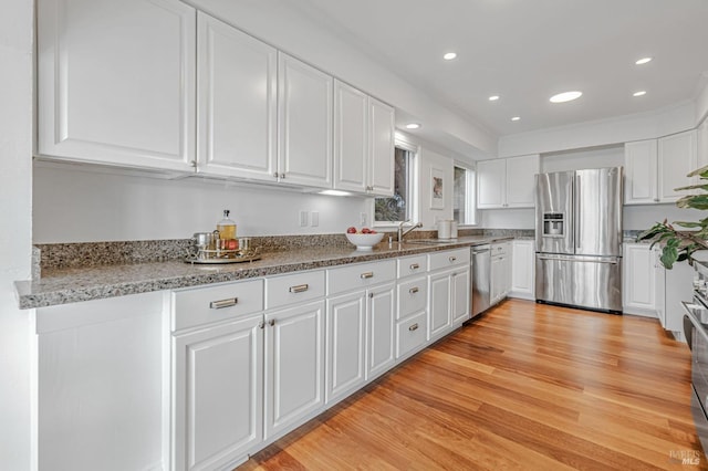 kitchen with light stone countertops, light wood-type flooring, white cabinetry, a sink, and stainless steel appliances