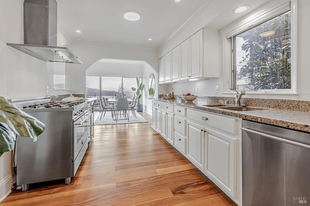 kitchen with island exhaust hood, appliances with stainless steel finishes, arched walkways, a sink, and white cabinetry