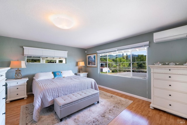 bedroom with an AC wall unit, baseboards, and light wood-style floors