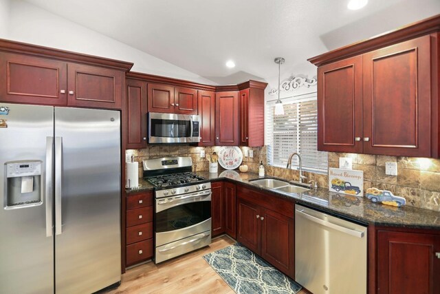 kitchen featuring appliances with stainless steel finishes, a sink, reddish brown cabinets, light wood-type flooring, and vaulted ceiling