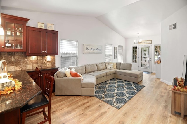 living room featuring an inviting chandelier, light wood-style floors, lofted ceiling, and visible vents