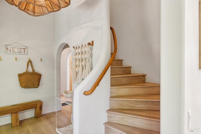 stairway featuring arched walkways and wood finished floors
