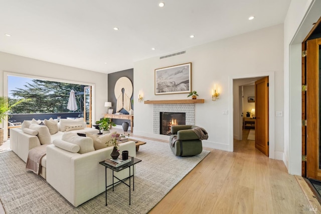 living room with visible vents, a glass covered fireplace, baseboards, recessed lighting, and light wood-style flooring