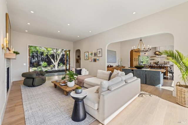 living area with a fireplace, light wood-style floors, recessed lighting, a chandelier, and arched walkways