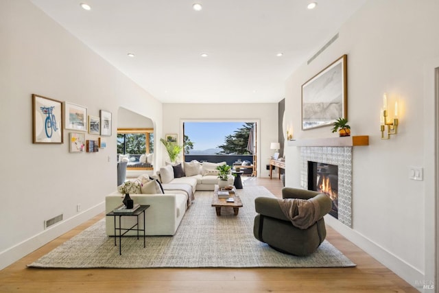 living area with a glass covered fireplace, recessed lighting, wood finished floors, and visible vents