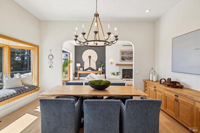 dining space featuring a fireplace, light wood-style floors, arched walkways, a chandelier, and recessed lighting