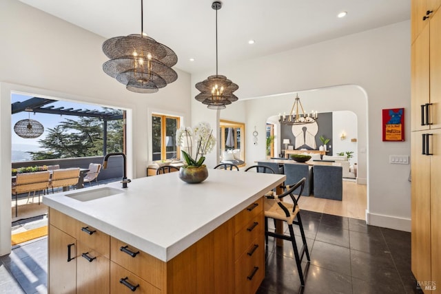 kitchen featuring arched walkways, a sink, light countertops, a chandelier, and an island with sink