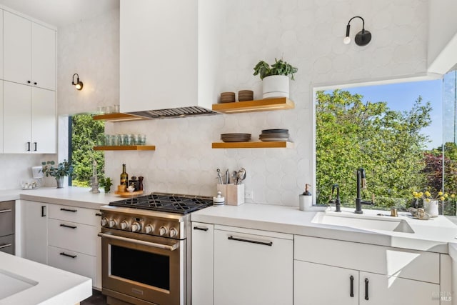 kitchen featuring open shelves, high end stainless steel range, a sink, light countertops, and decorative backsplash