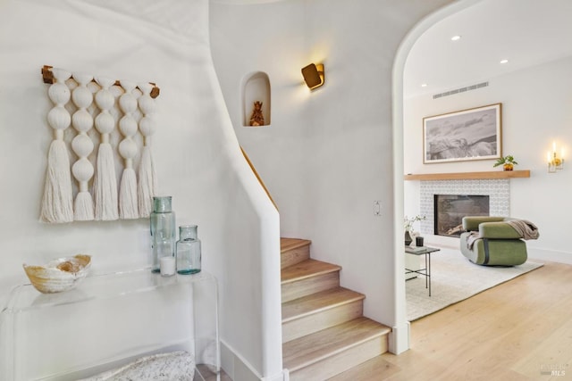 stairs with visible vents, arched walkways, wood finished floors, a glass covered fireplace, and recessed lighting