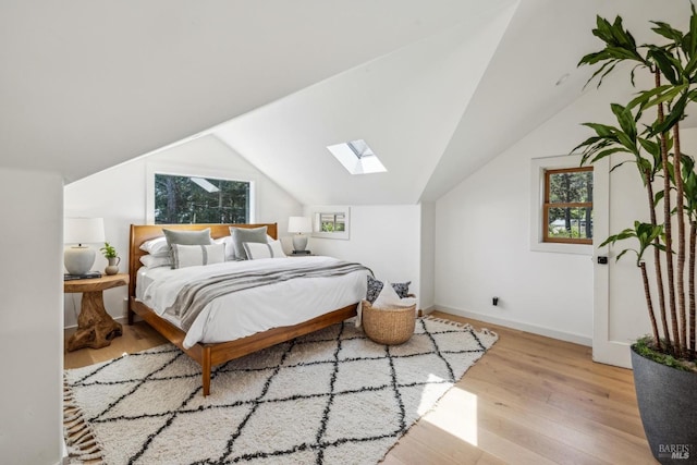 bedroom featuring vaulted ceiling with skylight, baseboards, and wood finished floors