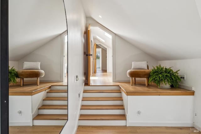 bonus room with wood finished floors, vaulted ceiling, and stairway