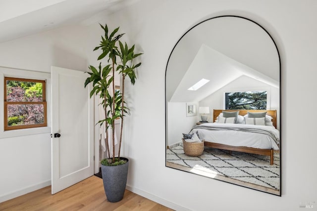 bedroom featuring multiple windows, light wood finished floors, and vaulted ceiling with skylight
