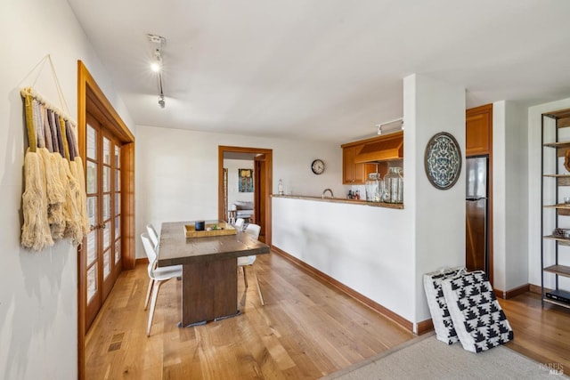 dining area with baseboards, rail lighting, and light wood-style flooring