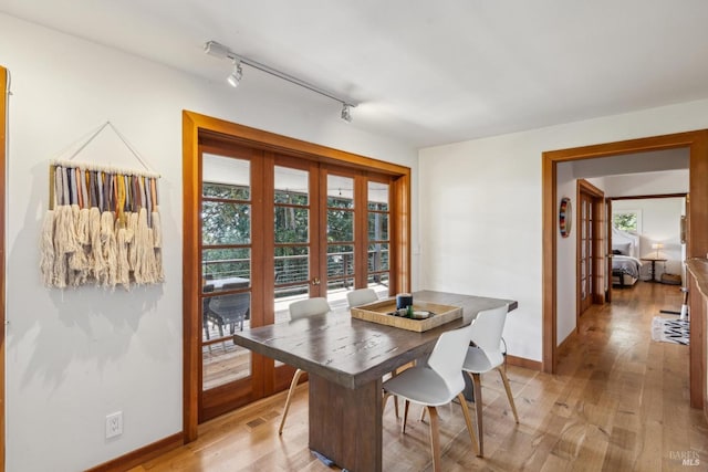 dining room featuring baseboards, french doors, rail lighting, and light wood-type flooring
