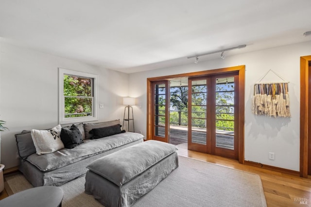 bedroom featuring baseboards, rail lighting, light wood-style flooring, and access to exterior