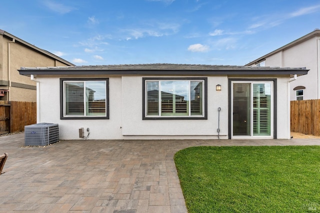 rear view of property with stucco siding, fence, a lawn, central air condition unit, and a patio area