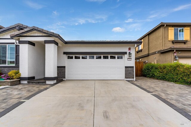 view of front of home featuring driveway, a tiled roof, an attached garage, stucco siding, and stone siding