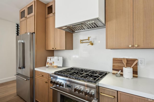 kitchen featuring wood finished floors, high end appliances, glass insert cabinets, light countertops, and custom range hood