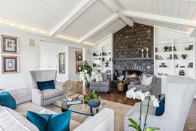 living area featuring vaulted ceiling with beams, built in shelves, wood finished floors, and a stone fireplace