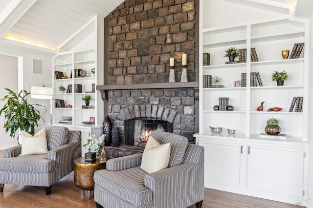 living area with wood finished floors, lofted ceiling, built in shelves, and a large fireplace