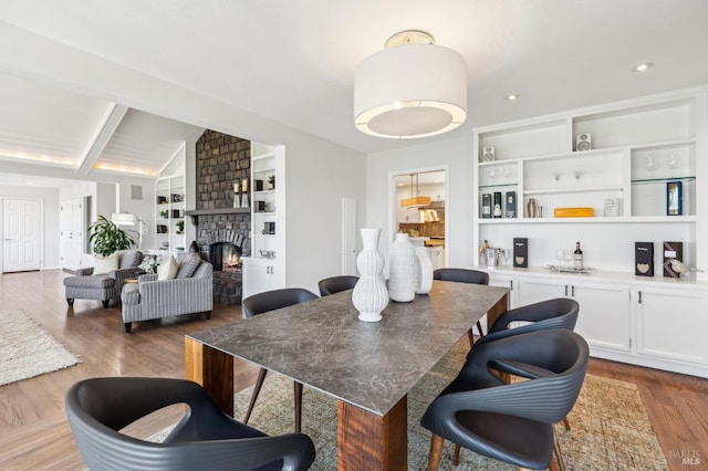 dining space featuring a fireplace, built in shelves, lofted ceiling with beams, and wood finished floors