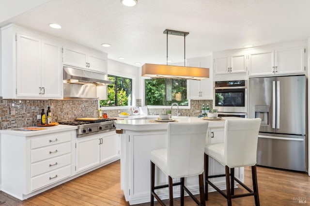 kitchen with light countertops, stainless steel appliances, white cabinetry, backsplash, and under cabinet range hood