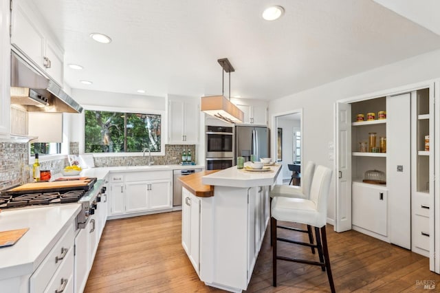 kitchen with a kitchen bar, white cabinets, a sink, light wood-style flooring, and appliances with stainless steel finishes