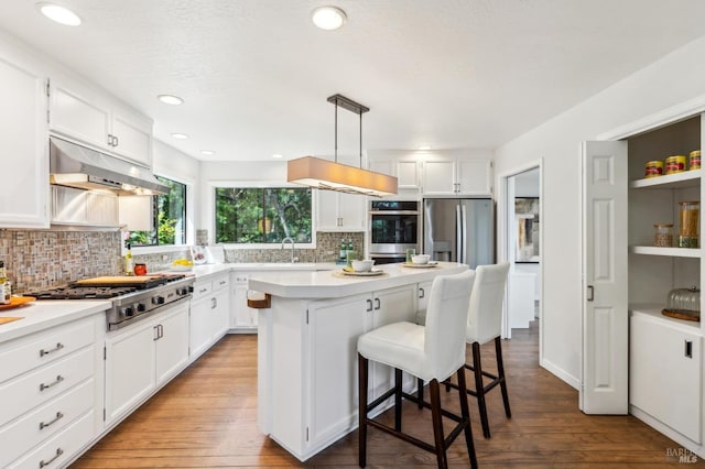 kitchen with appliances with stainless steel finishes, a breakfast bar area, under cabinet range hood, and white cabinetry