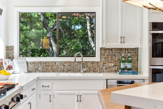kitchen featuring white cabinets, a sink, light countertops, stainless steel appliances, and tasteful backsplash
