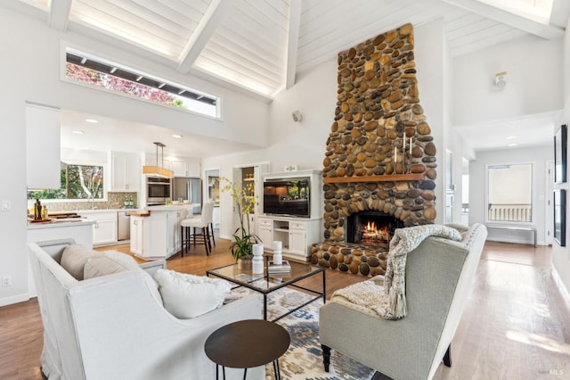 living room featuring a fireplace, high vaulted ceiling, baseboards, beamed ceiling, and light wood-style flooring